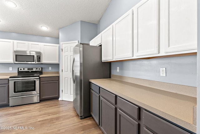 kitchen with gray cabinetry, a textured ceiling, stainless steel appliances, light wood-style floors, and light countertops