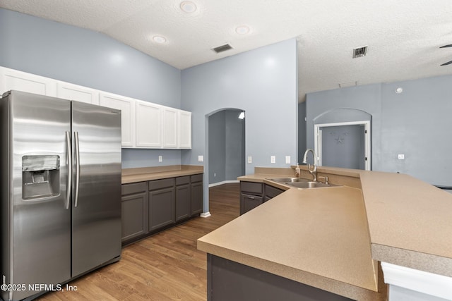 kitchen with visible vents, light wood-style floors, arched walkways, stainless steel fridge, and a sink