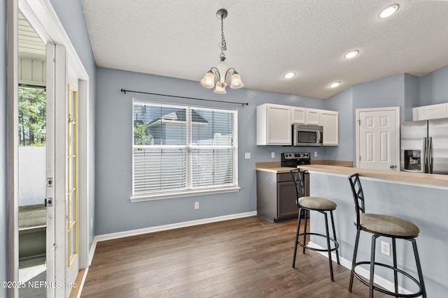 kitchen featuring a healthy amount of sunlight, a breakfast bar, dark wood finished floors, appliances with stainless steel finishes, and a notable chandelier