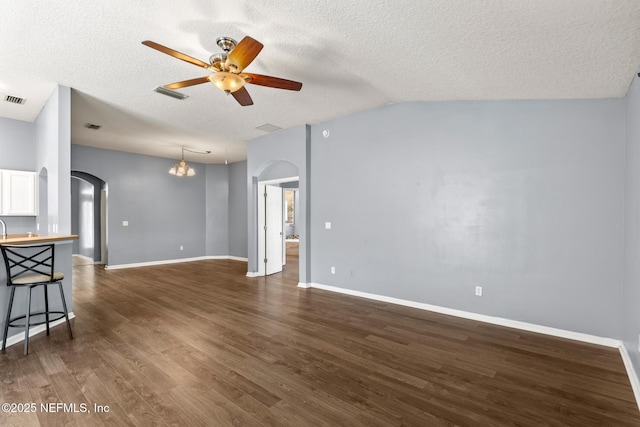 living area featuring dark wood-type flooring, ceiling fan with notable chandelier, a textured ceiling, arched walkways, and baseboards