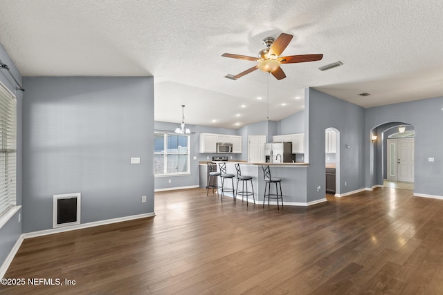 unfurnished living room featuring visible vents, ceiling fan with notable chandelier, dark wood finished floors, arched walkways, and lofted ceiling