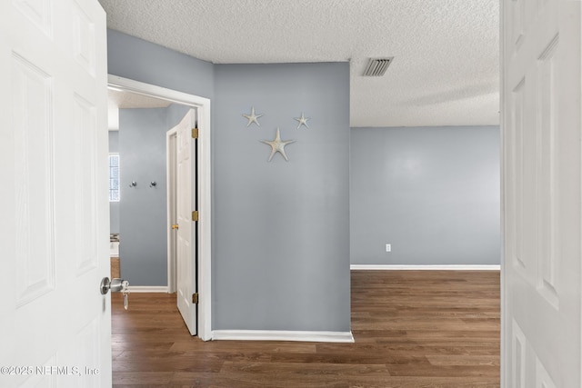 corridor featuring visible vents, a textured ceiling, baseboards, and wood finished floors