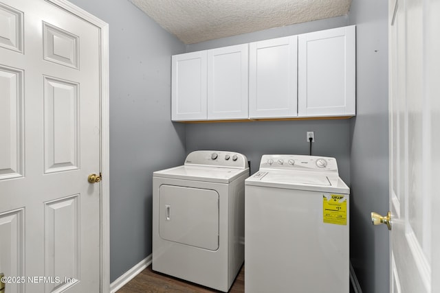 washroom featuring a textured ceiling, washing machine and dryer, dark wood finished floors, cabinet space, and baseboards