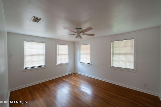 empty room featuring a ceiling fan, wood finished floors, visible vents, and baseboards