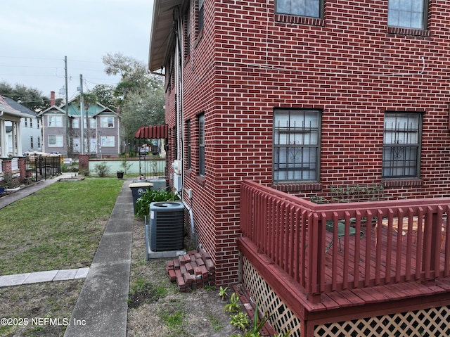 view of property exterior with central air condition unit, brick siding, and a lawn