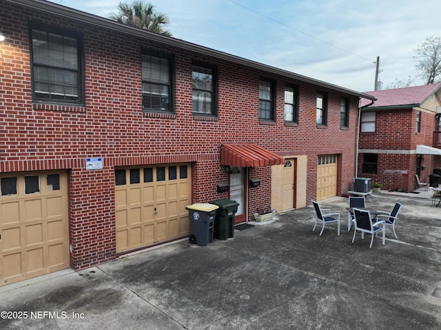 rear view of house featuring cooling unit, brick siding, a garage, and driveway