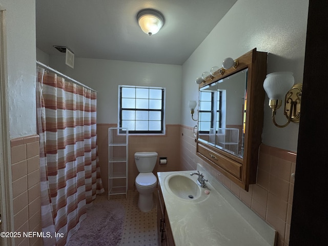 bathroom with tile walls, a wainscoted wall, toilet, a shower with curtain, and vanity