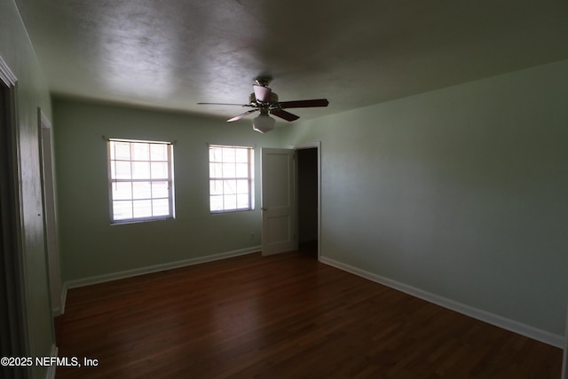 unfurnished room featuring dark wood finished floors, baseboards, and ceiling fan