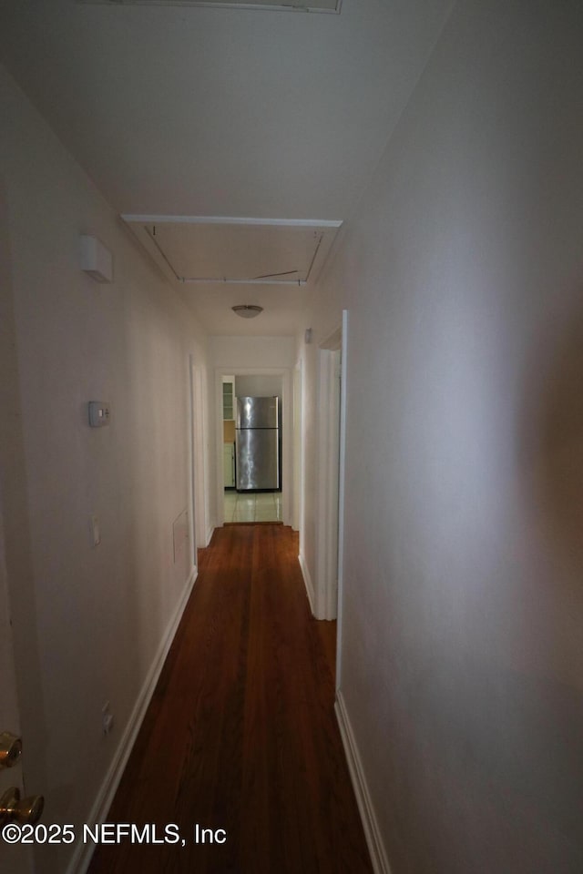 corridor featuring baseboards, attic access, and dark wood finished floors