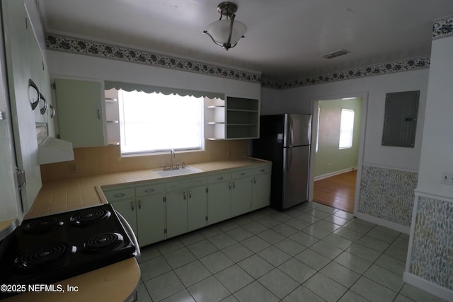 kitchen with electric panel, freestanding refrigerator, a sink, tile counters, and electric stove