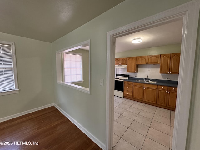 kitchen featuring a sink, tasteful backsplash, dark countertops, white electric stove, and baseboards