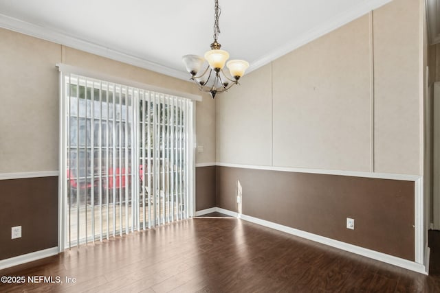 spare room featuring an inviting chandelier, wood finished floors, baseboards, and ornamental molding