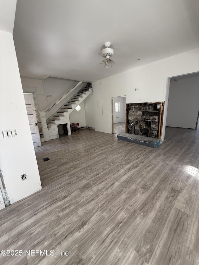 unfurnished living room featuring a stone fireplace, stairway, wood finished floors, and ceiling fan