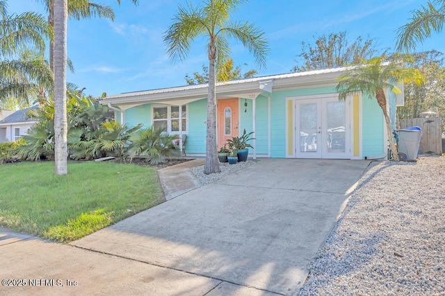 ranch-style home with fence, covered porch, a front lawn, concrete driveway, and french doors