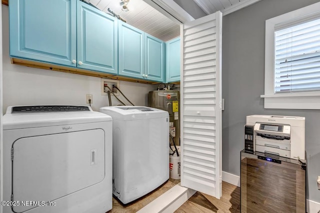 clothes washing area featuring washing machine and dryer, water heater, cabinet space, light wood finished floors, and baseboards