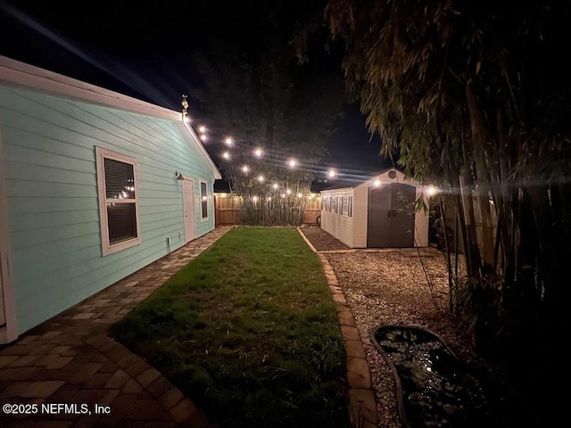 yard at night featuring an outbuilding, a storage unit, and a fenced backyard