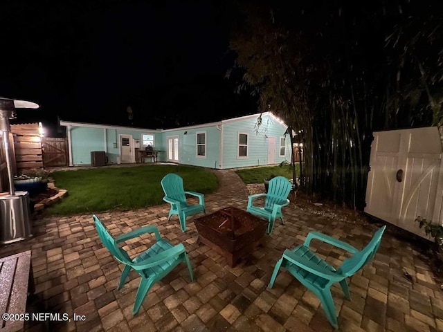 patio at night with fence, a lawn, and a fire pit