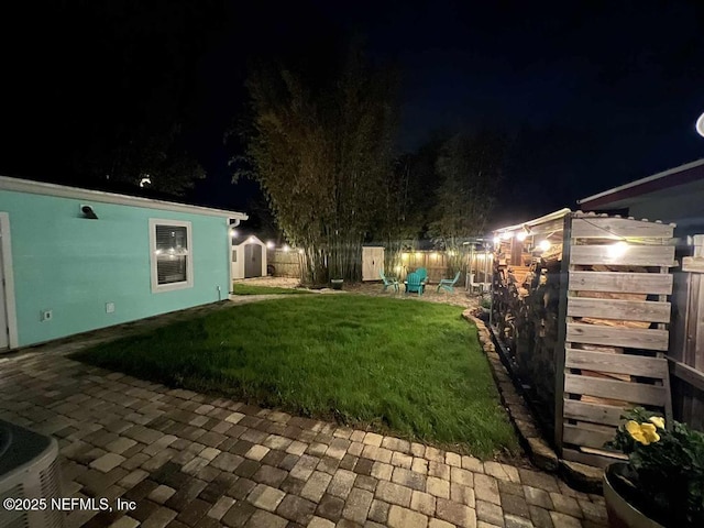 yard at night with a storage shed, an outbuilding, and a fenced backyard