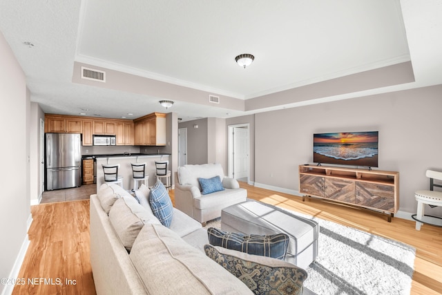 living area featuring visible vents, baseboards, a raised ceiling, and light wood-style floors