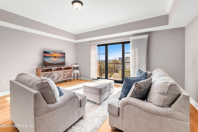 living area featuring a tray ceiling, crown molding, baseboards, and light wood-type flooring