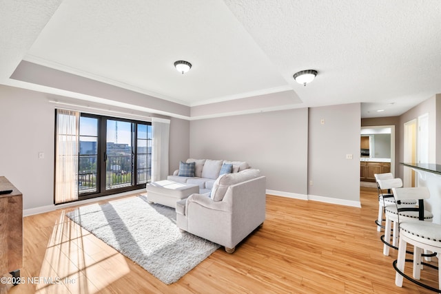 living area with a tray ceiling, a textured ceiling, light wood-type flooring, and baseboards