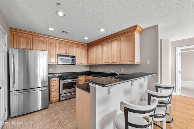 kitchen with visible vents, a breakfast bar, dark countertops, stainless steel appliances, and a peninsula