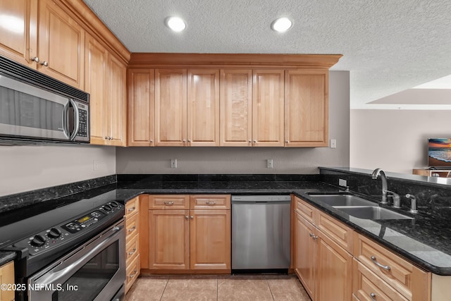 kitchen with light tile patterned floors, a peninsula, a sink, appliances with stainless steel finishes, and a textured ceiling