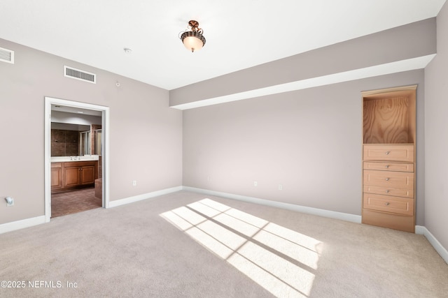 unfurnished bedroom with light carpet, visible vents, ensuite bath, and baseboards