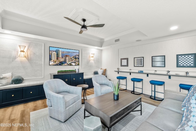 living area featuring visible vents, light wood-style floors, ceiling fan, and ornamental molding