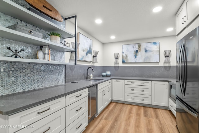 kitchen with backsplash, open shelves, freestanding refrigerator, light wood-style floors, and a sink