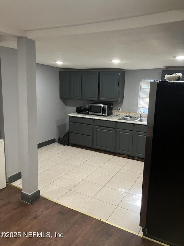 kitchen with light wood finished floors, a sink, gray cabinetry, light countertops, and stainless steel appliances