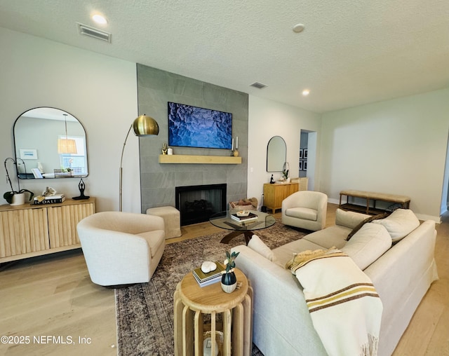 living area featuring visible vents, a textured ceiling, wood finished floors, and a tile fireplace