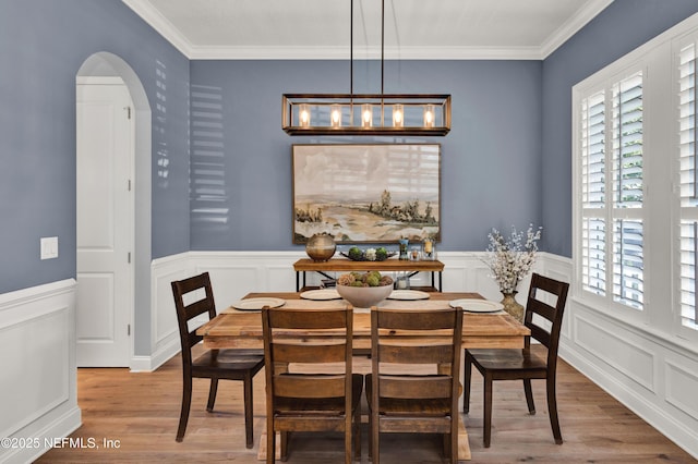 dining area featuring crown molding, wainscoting, wood finished floors, and arched walkways