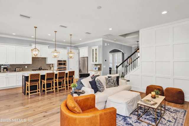 living area featuring crown molding, light wood-style floors, stairway, a decorative wall, and arched walkways