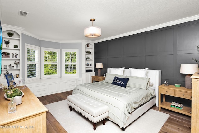 bedroom with a decorative wall, visible vents, ornamental molding, and wood finished floors