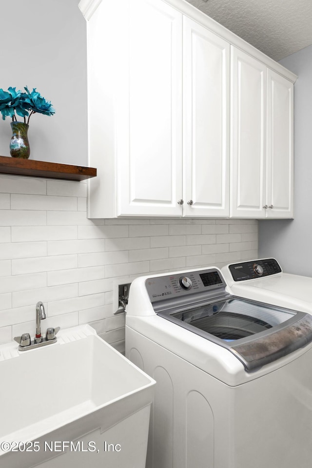 laundry room with cabinet space, a textured ceiling, a sink, and separate washer and dryer