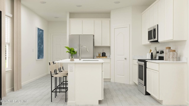 kitchen with a center island with sink, a kitchen bar, light countertops, appliances with stainless steel finishes, and white cabinetry