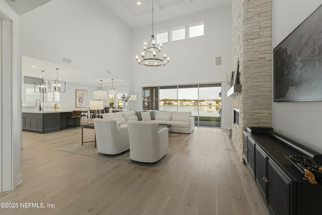 living room featuring a stone fireplace, a notable chandelier, visible vents, and light wood-type flooring