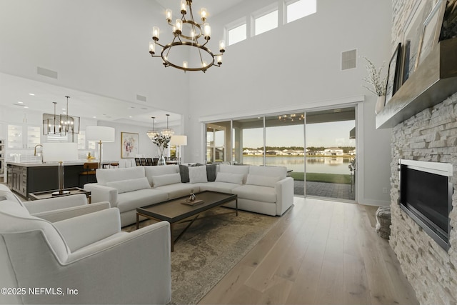 living area with light wood-type flooring, a water view, visible vents, a stone fireplace, and an inviting chandelier