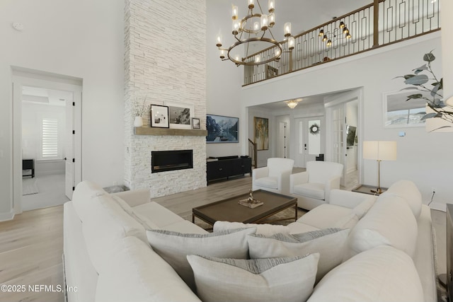 living room with a notable chandelier, a fireplace, a high ceiling, and light wood-style floors