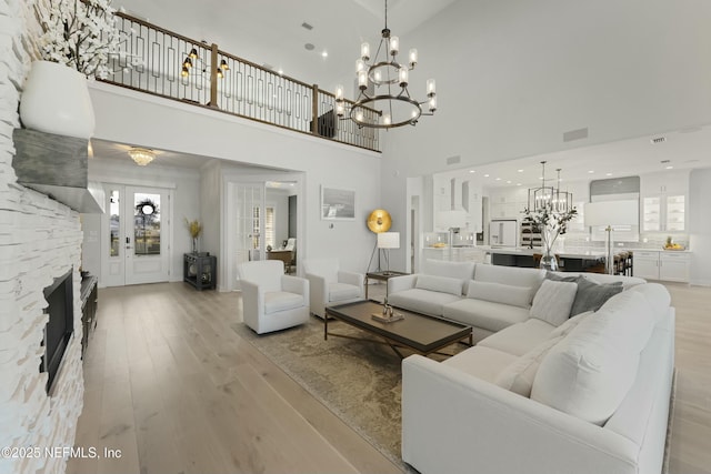 living room with a stone fireplace, an inviting chandelier, light wood-style flooring, and a healthy amount of sunlight