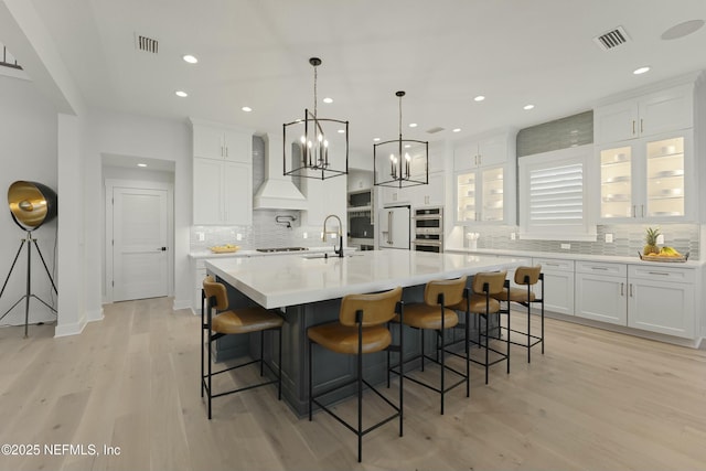 kitchen featuring custom exhaust hood, a notable chandelier, white cabinetry, and light wood-style floors