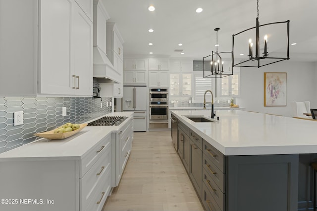 kitchen with gray cabinets, a sink, light countertops, appliances with stainless steel finishes, and a notable chandelier