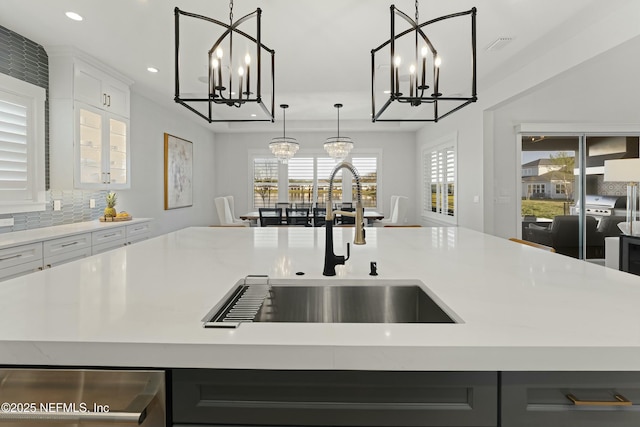 kitchen with decorative backsplash, a notable chandelier, a center island with sink, and a sink