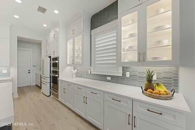 kitchen featuring a warming drawer, visible vents, white cabinetry, light wood finished floors, and light countertops