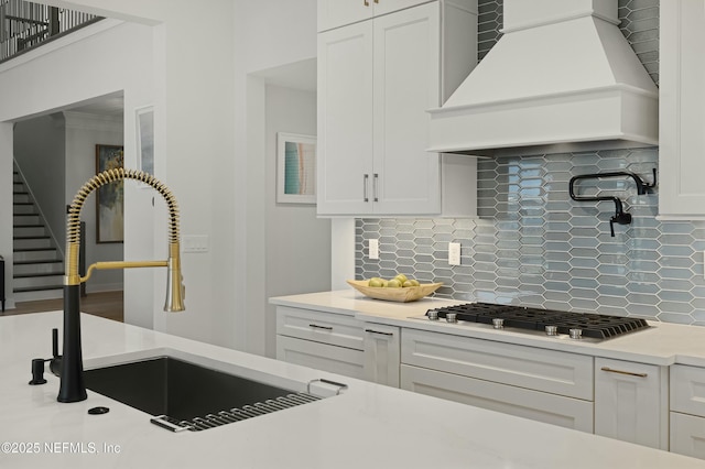 kitchen with a sink, white cabinetry, stainless steel gas stovetop, and custom range hood