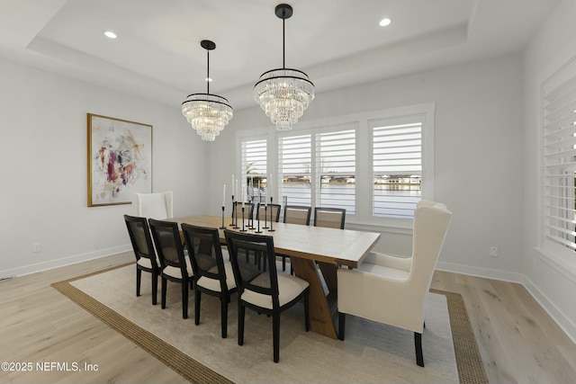 dining space with baseboards, a raised ceiling, and light wood-style flooring