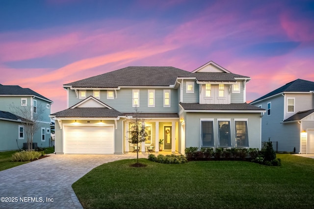 view of front of home featuring a lawn, decorative driveway, cooling unit, roof with shingles, and a garage