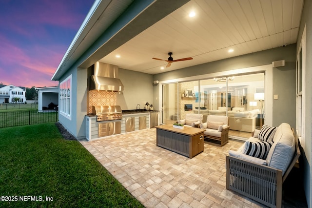 patio terrace at dusk featuring area for grilling, a ceiling fan, fence, exterior kitchen, and outdoor lounge area