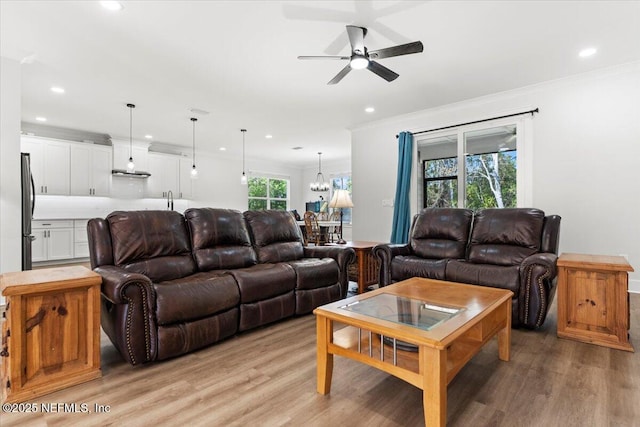 living room with recessed lighting, light wood-style floors, crown molding, and ceiling fan with notable chandelier